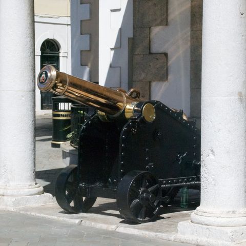 A polished brass cannon on a black iron carriage, framed by white stone columns.